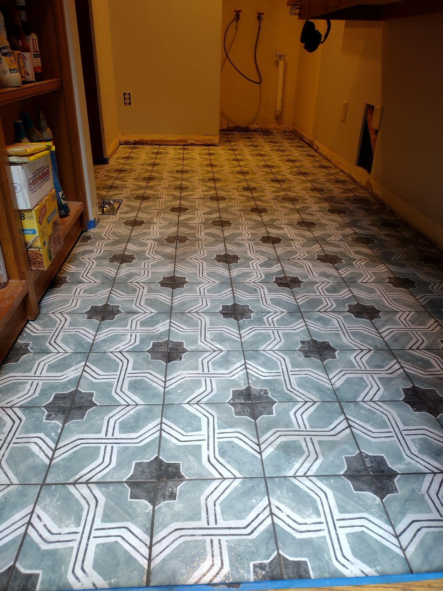 A tiled floor with a geometric pattern is being painted in a kitchen.