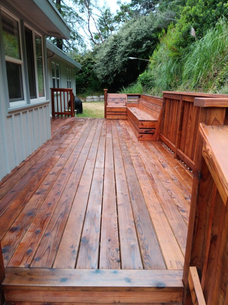 A wooden deck with a bench and stairs in front of a house.