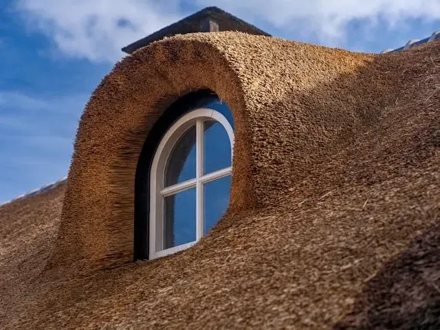 Close-up of a traditional thatched roof window with textured natural roofing material and curved architectural detail. 
