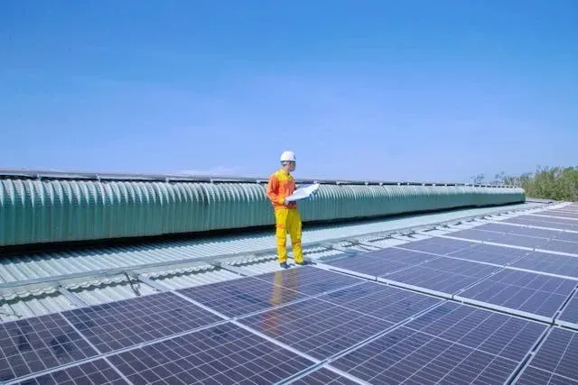 Worker inspecting rooftop solar panels installed on a commercial metal roof under a clear blue sky. 