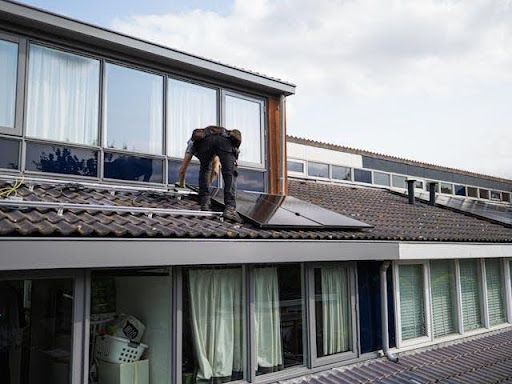 Professional roofer installing or repairing a tiled residential roof on a modern house exterior.