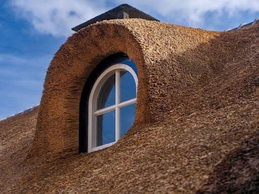Close-up of a traditional thatched roof window with textured natural roofing material and curved architectural detail.