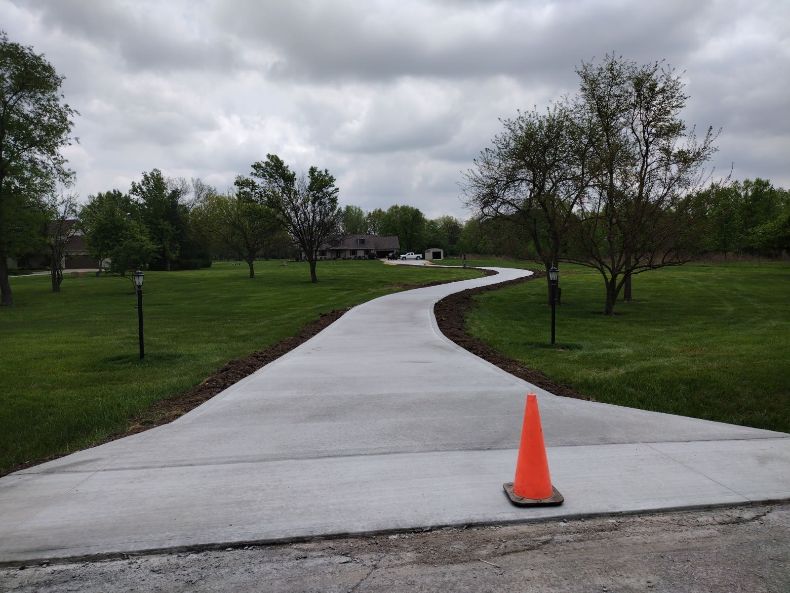 A concrete driveway with an orange cone on the side