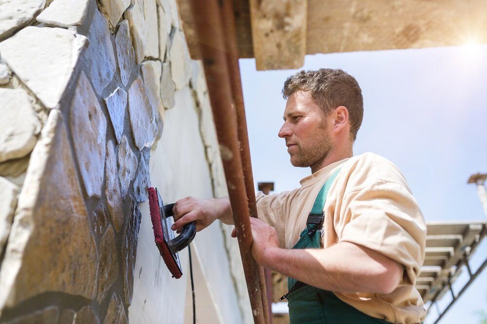 A Man Is Working On A Stone Wall With A Trowel — JGA Concreting Pty Ltd In Berrimah, NT