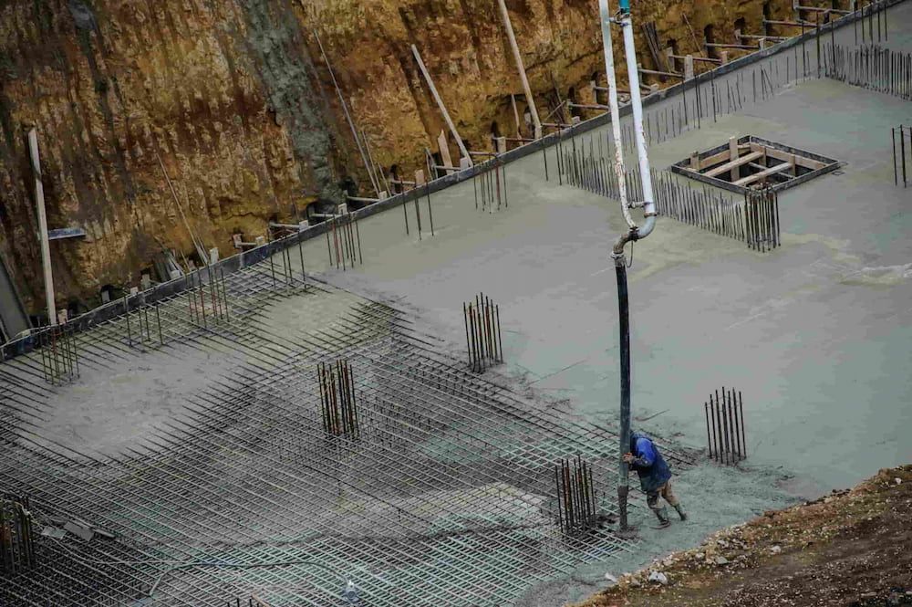 A Man Is Pouring Concrete Into A Hole In The Ground — JGA Concreting Pty Ltd In Berrimah, NT