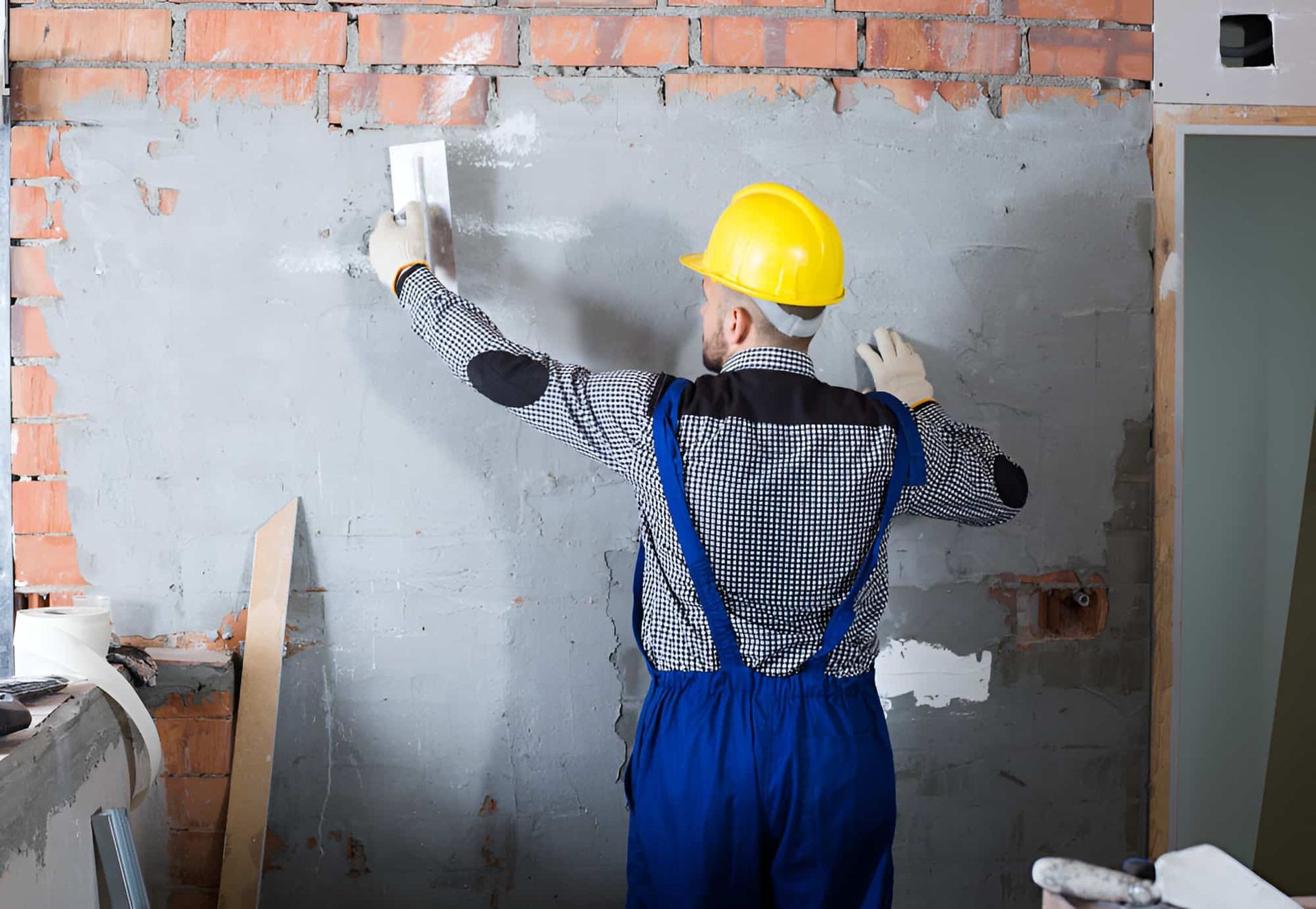 A Man In A Hard Hat Is Plastering A Wall — JGA Concreting Pty Ltd In Berrimah, NT