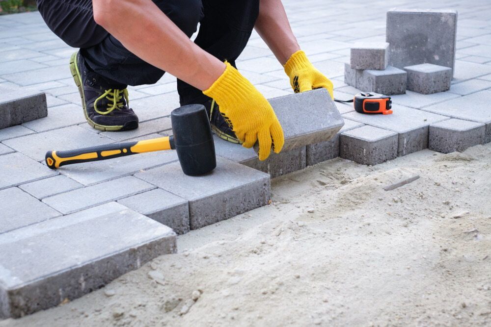 A Man Is Laying Bricks On A Patio With A Rubber Mallet — JGA Concreting Pty Ltd In Berrimah, NT
