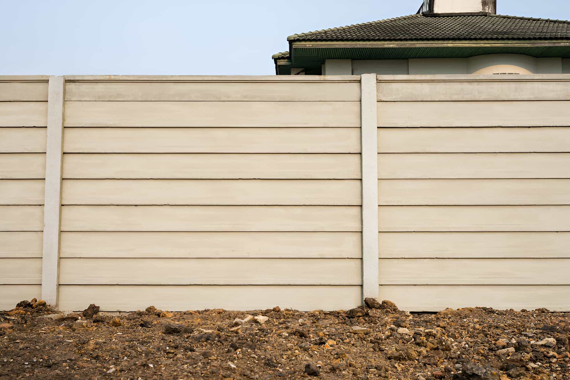 A Concrete Fence Surrounds A Dirt Field With A House In The Background — JGA Concreting Pty Ltd In Berrimah, NT