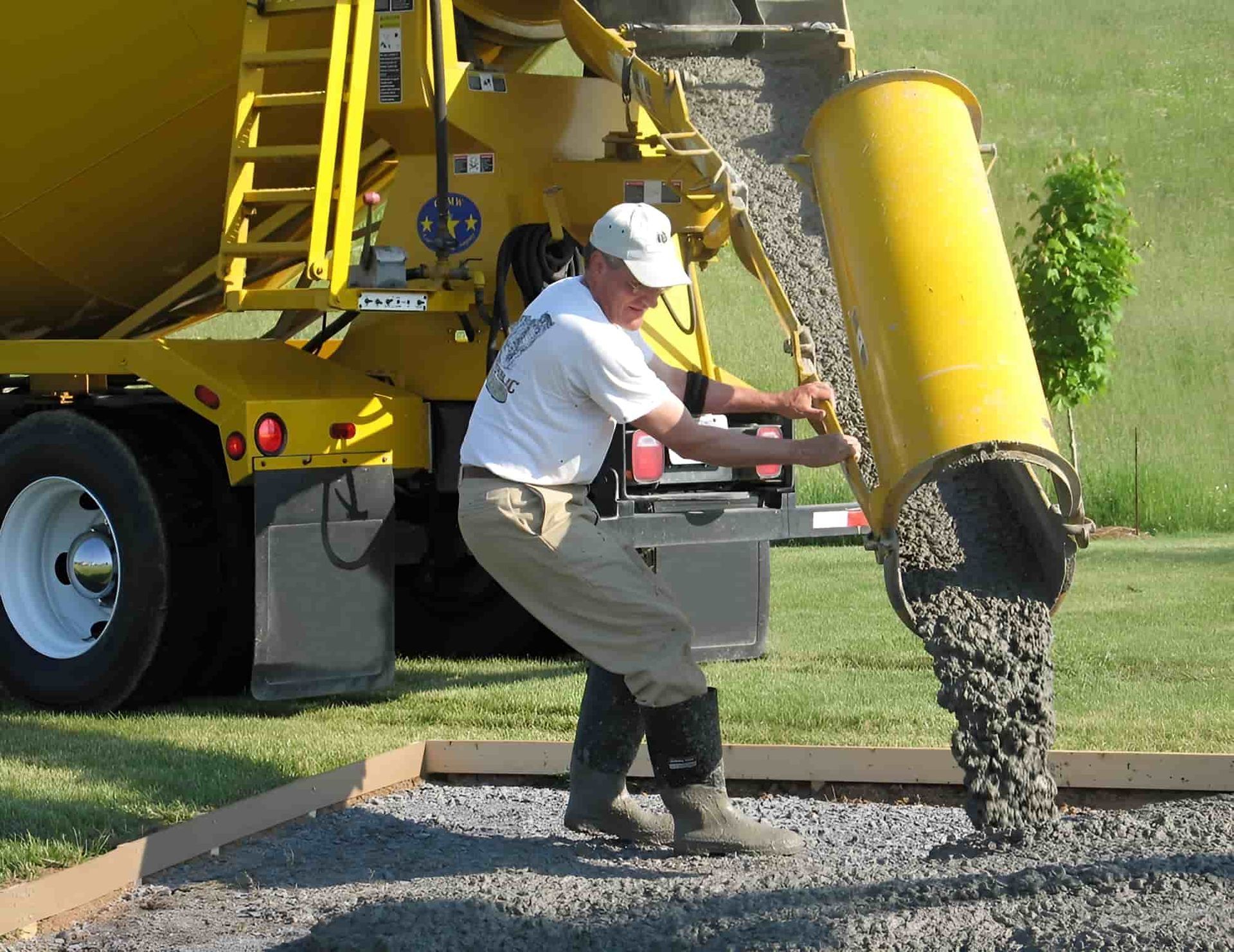 A Man Is Pouring Concrete From A Yellow Truck — JGA Concreting Pty Ltd In Berrimah, NT