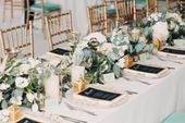 Elegant wedding table setting with gold chairs, floral arrangements, eucalyptus, green glassware, and black menus.