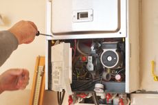 Person repairs a gas boiler with a screwdriver; indoor setting.