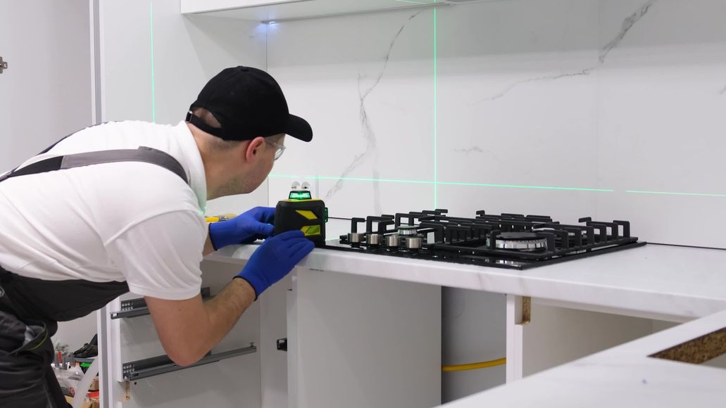 A person in a kitchen using a laser level to install a countertop.