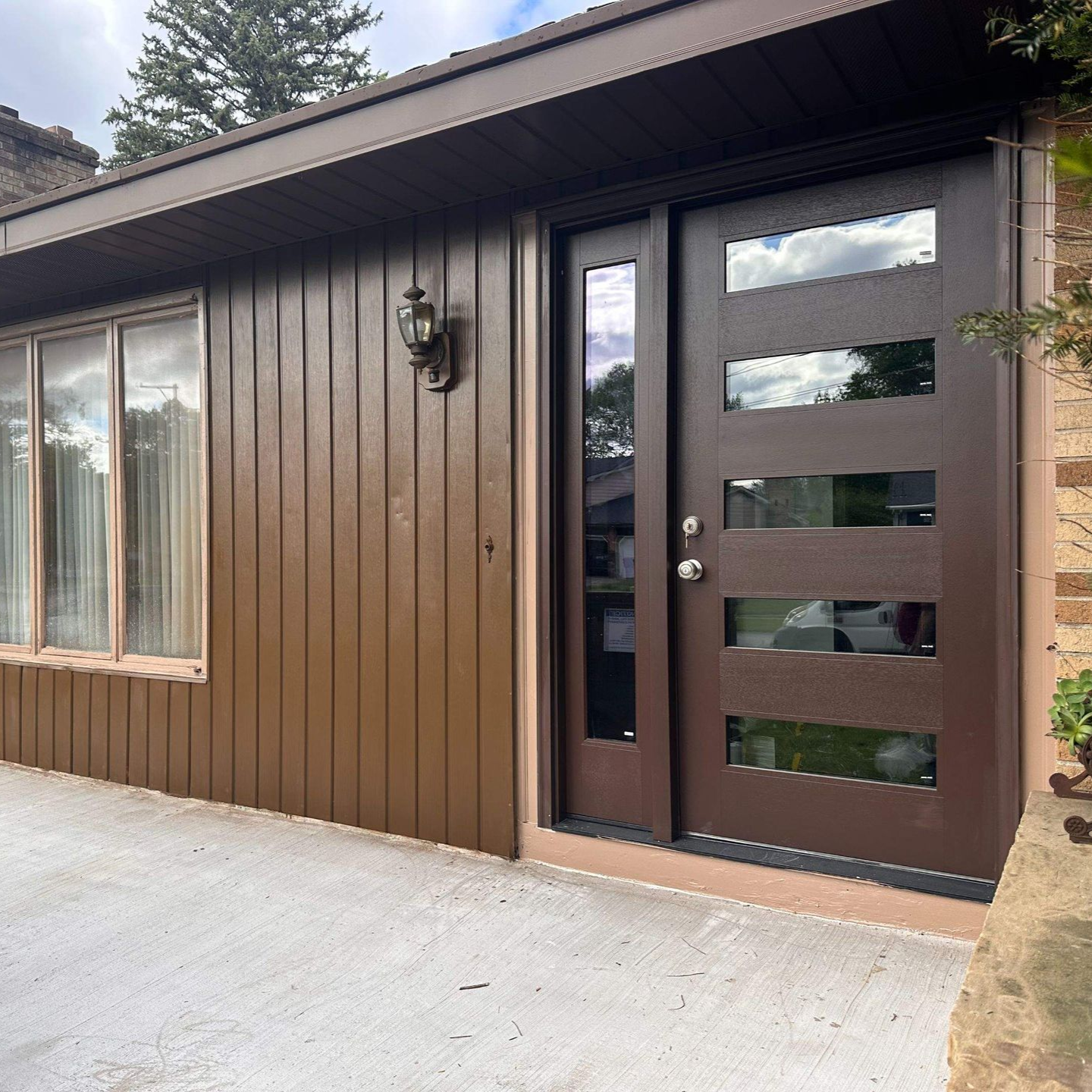 Brown house exterior with a modern front door, sidelight, and windows.