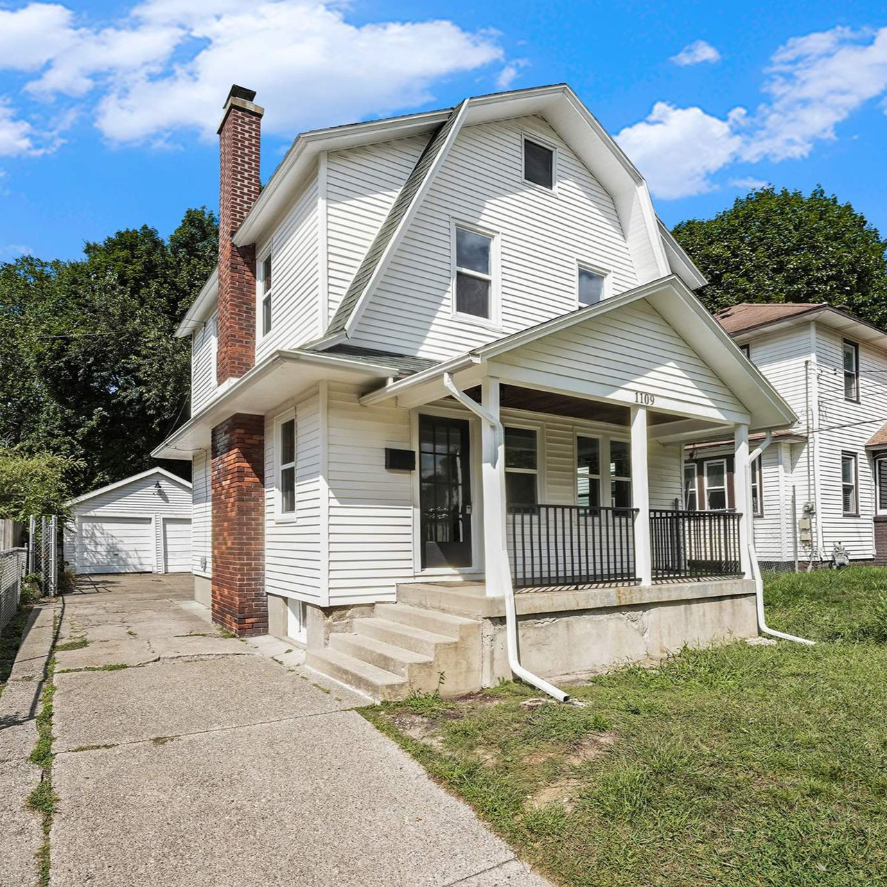 White two-story house with brick chimney, porch, and attached garage on a sunny day.