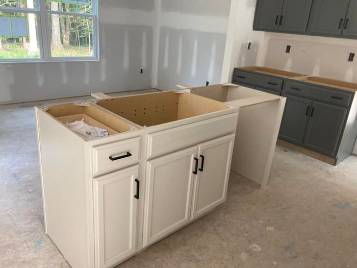 A kitchen under construction with white cabinets and gray cabinets.