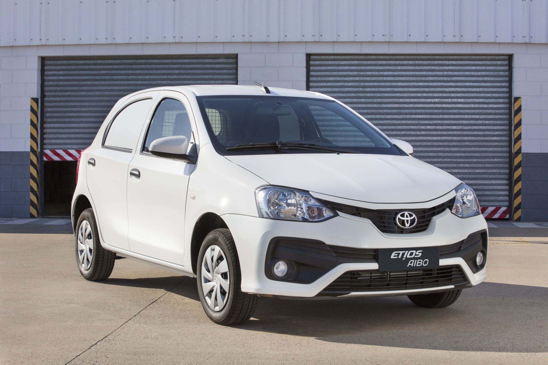 Un Toyota Etios blanco está estacionado frente a una puerta de garaje.