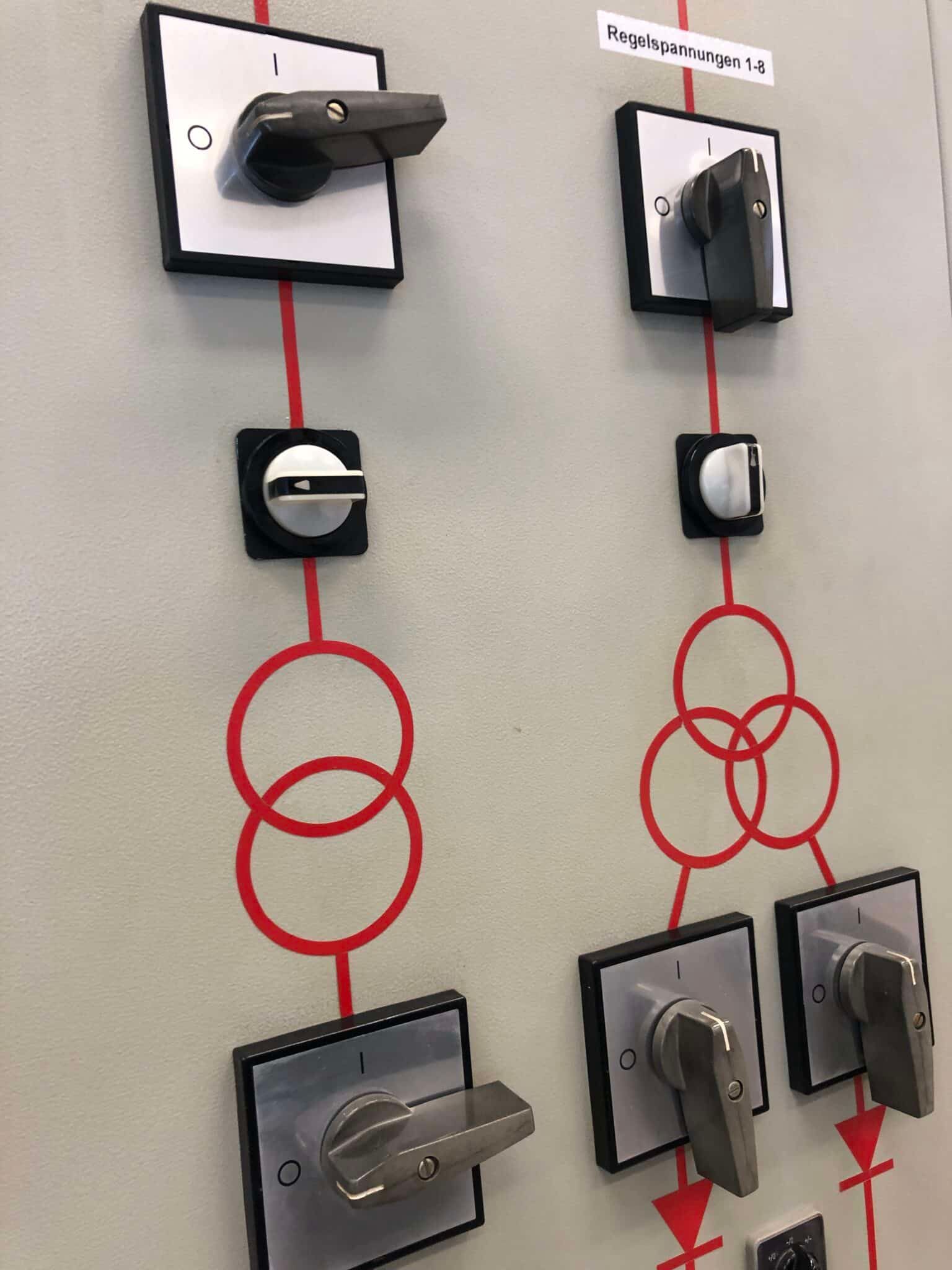 Grauer Schaltschrank mit mehreren schwarzen und grauen Drehschaltern als Symbol für Spannung