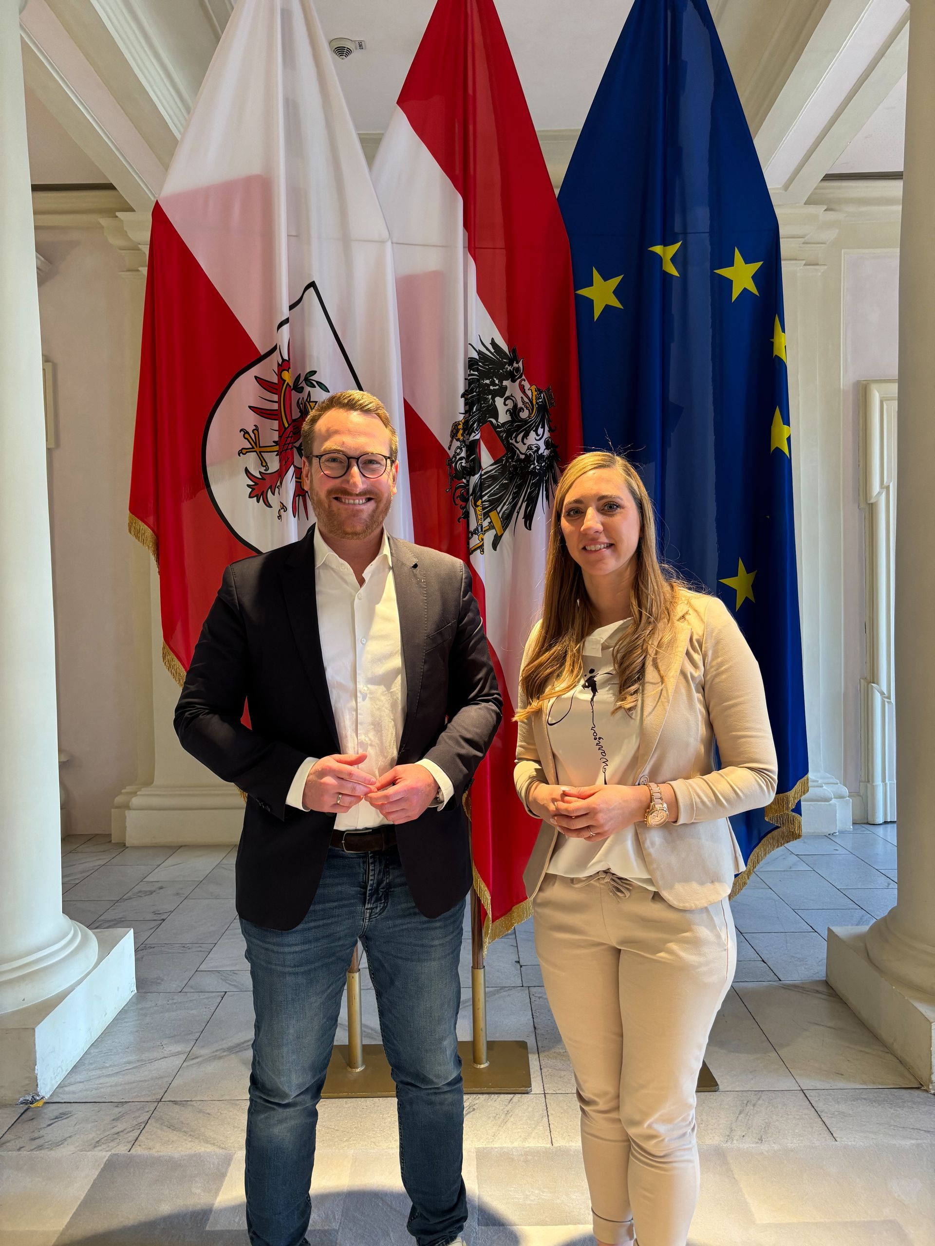  Landeshauptmann-Stellvertreter Philip Wohlgemuth, Land Tirol und Melanie Spangler, Geschäftsführerin arbeit plus Tirol vor der Tiroler, der österreichischen und europäischen Flagge. 