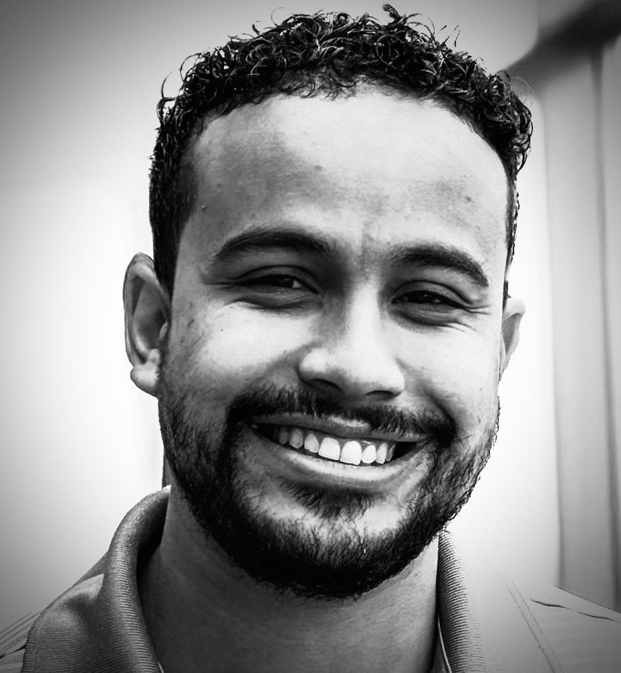 A man wearing sunglasses and a plaid shirt is smiling.