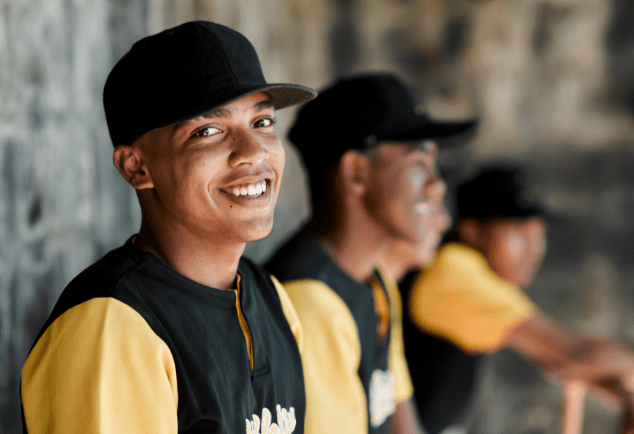 A group of baseball players are sitting in a dugout and smiling.