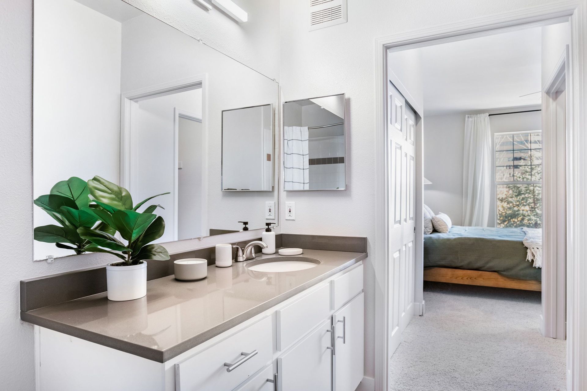 Bathroom with white cabinets, grey countertop, and a plant. Bedroom visible in the background at The Viridian in Greenwood Village, CO.