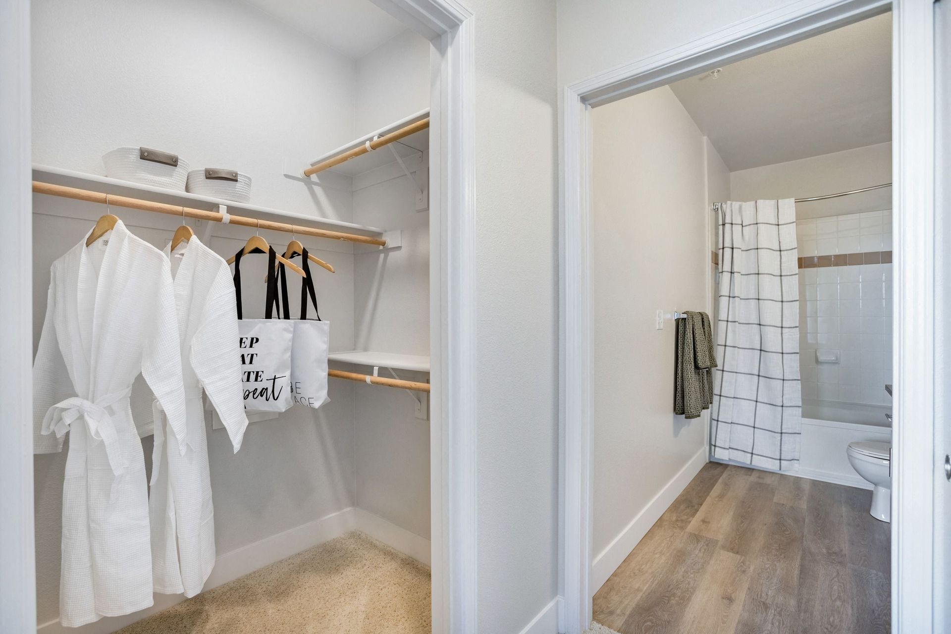 Walk-in closet with robes and a bathroom doorway, light-colored walls and flooring at The Viridian in Greenwood Village, CO.
