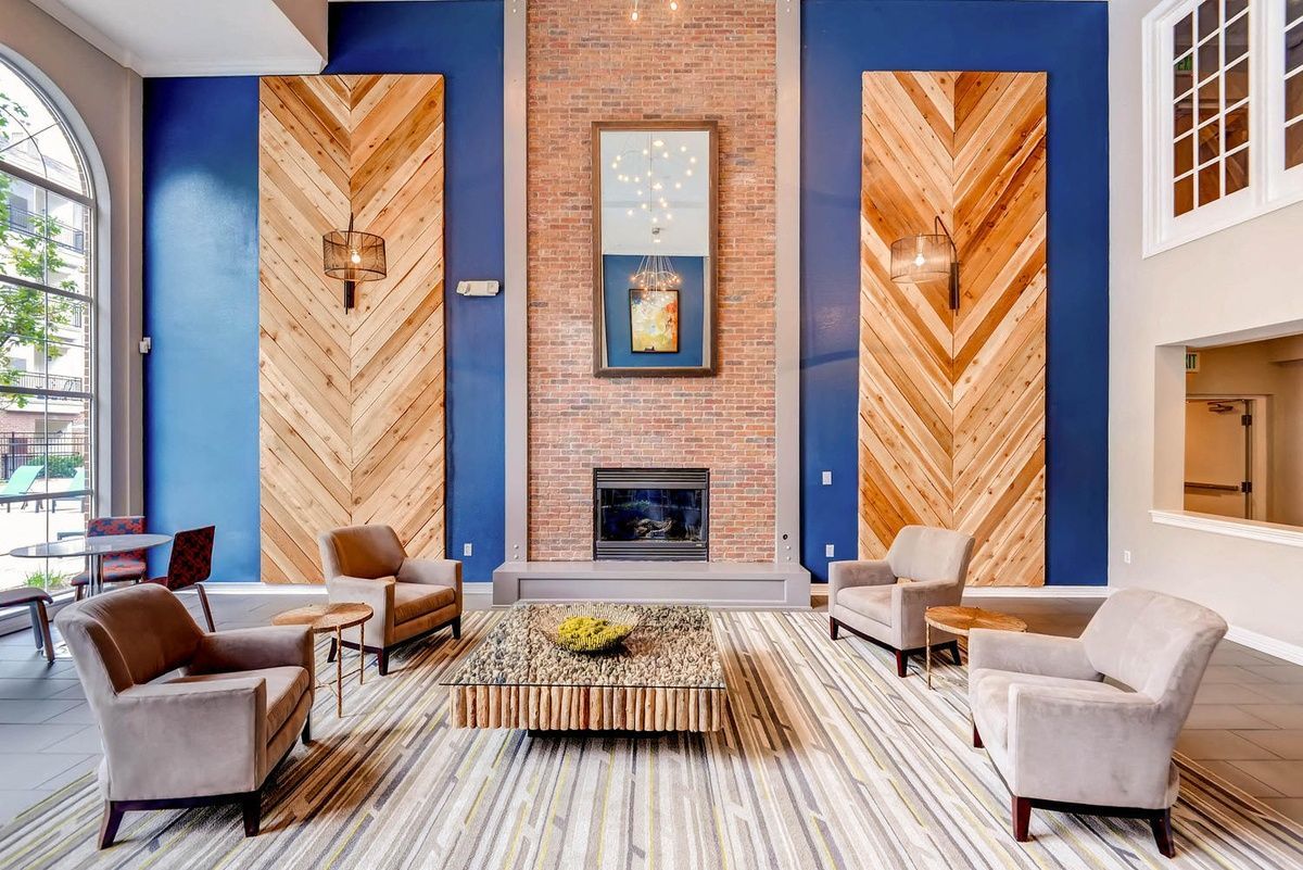 Lounge with blue wall, brick fireplace, chevron wood panels, neutral armchairs, and striped rug at The Viridian in Greenwood Village, CO.