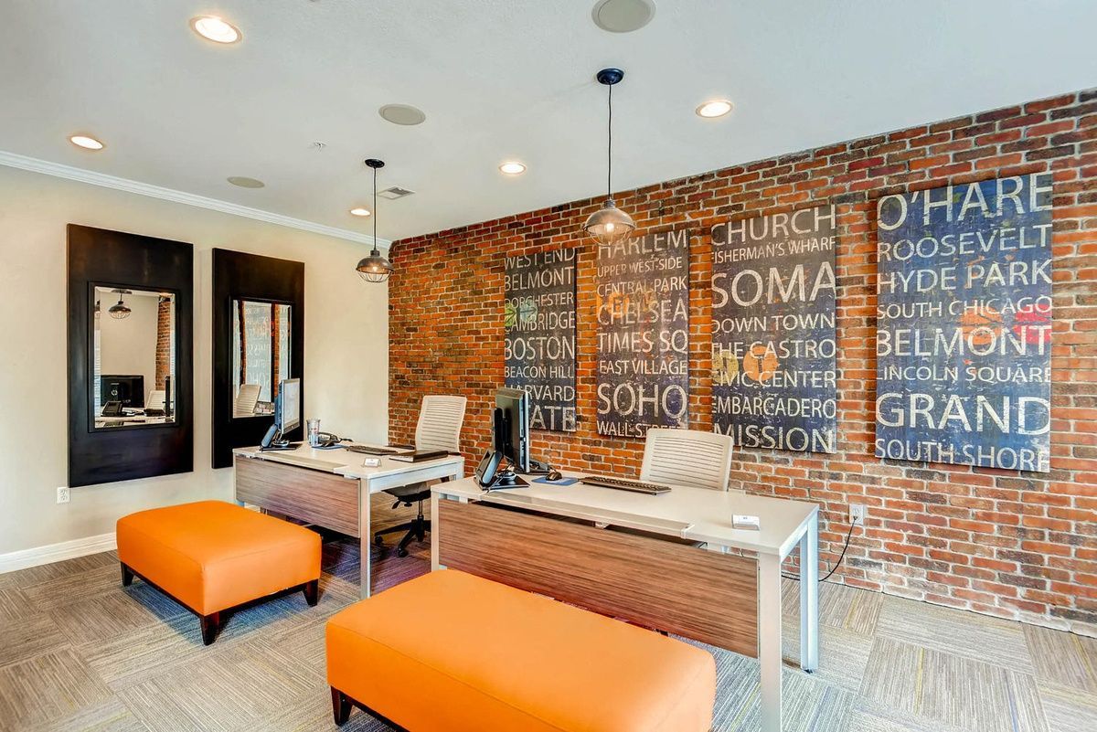 Office reception area with brick accent wall, desks, orange ottomans at The Viridian in Greenwood Village, CO.