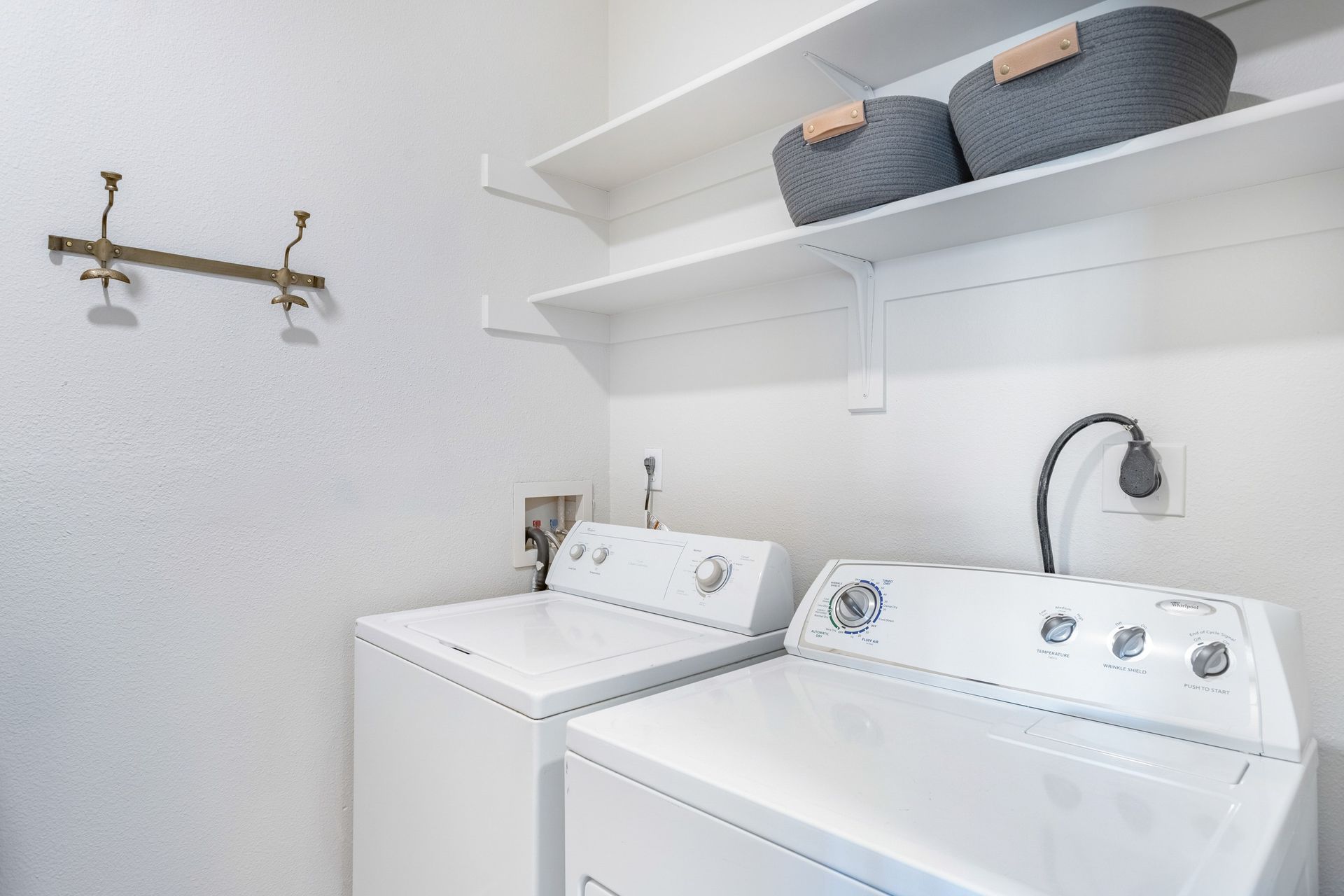White laundry room with washer, dryer, shelves with baskets, and coat rack at The Viridian in Greenwood Village, CO.