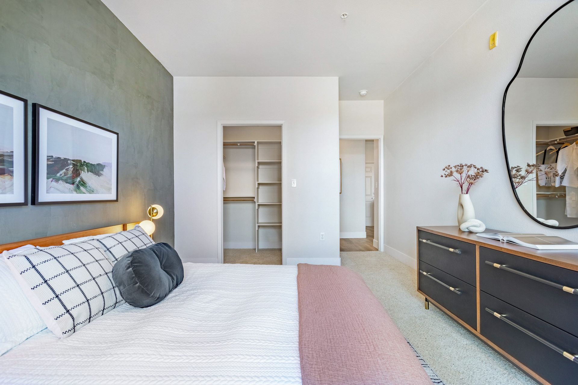 Bedroom with a bed, dresser, and wall art. Features a walk-in closet and an arched mirror at The Viridian in Greenwood Village, CO.