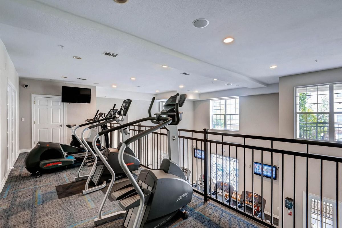 Gym with elliptical machines on a mezzanine level overlooking the room below. Black railing, carpet at The Viridian in Greenwood Village, CO.