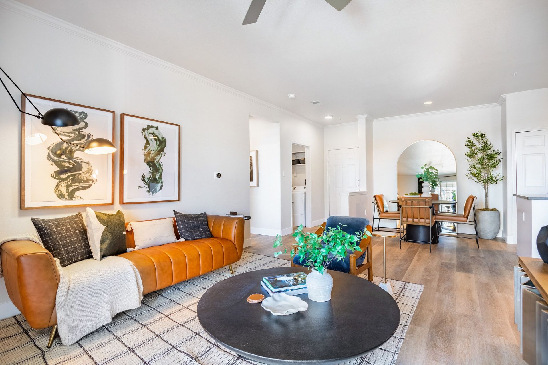 A bright, modern living room with brown leather sofa, round coffee table, and dining area at The Viridian in Greenwood Village, CO.