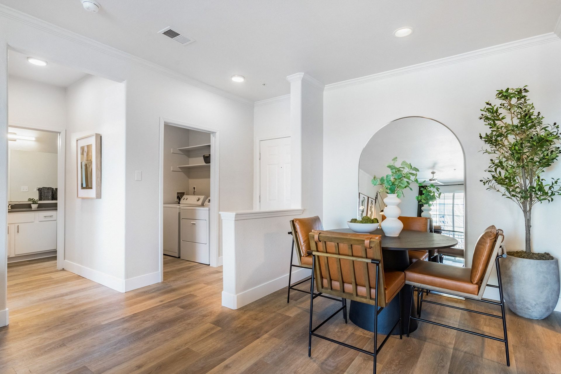 Dining room with wooden floors, table, leather chairs, and large mirror.