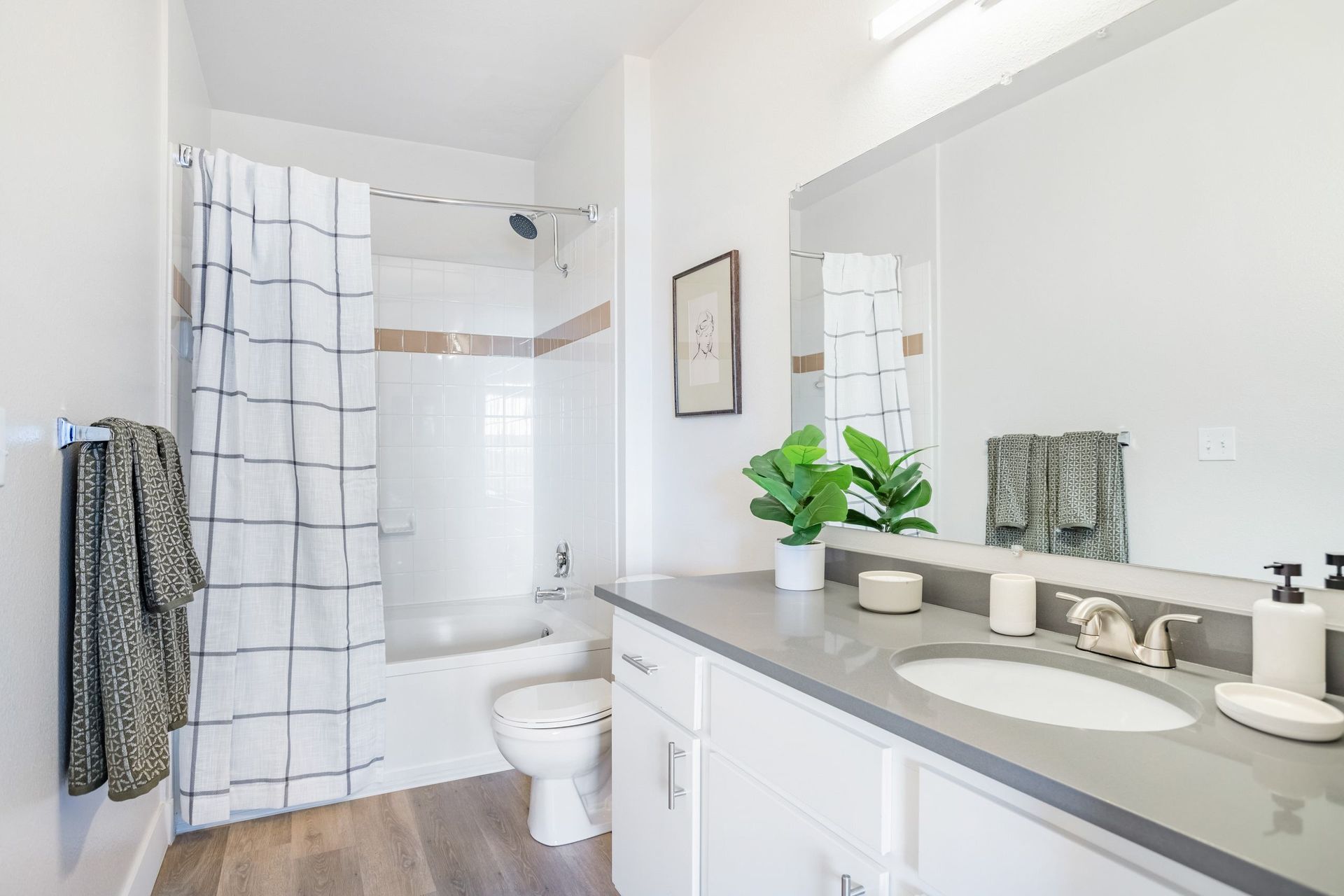Bathroom with white cabinets, gray countertop, a shower/tub with a plaid curtain, and a large mirror at The Viridian in Greenwood Village, CO.