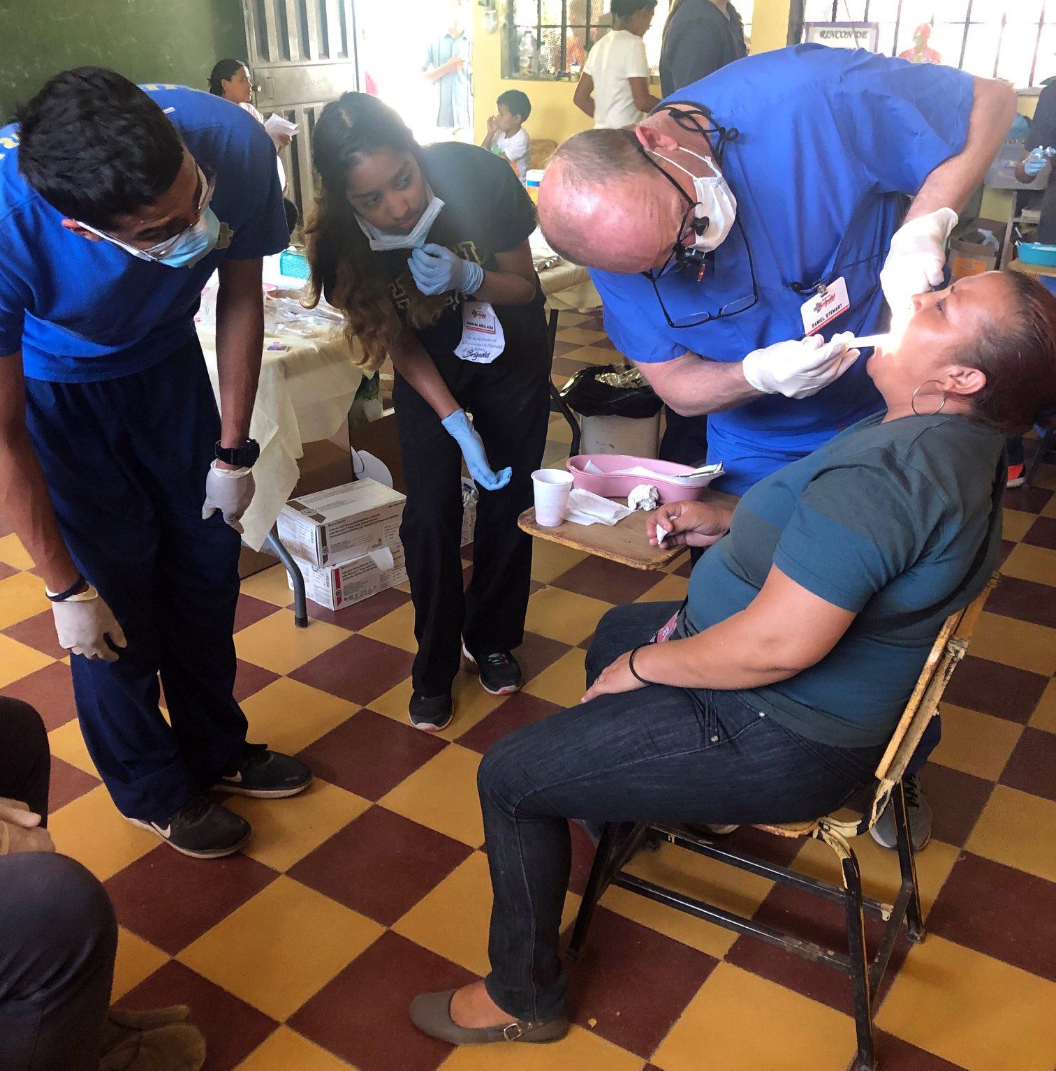Dentists examining a woman's teeth in a clinic. Other people in the background.