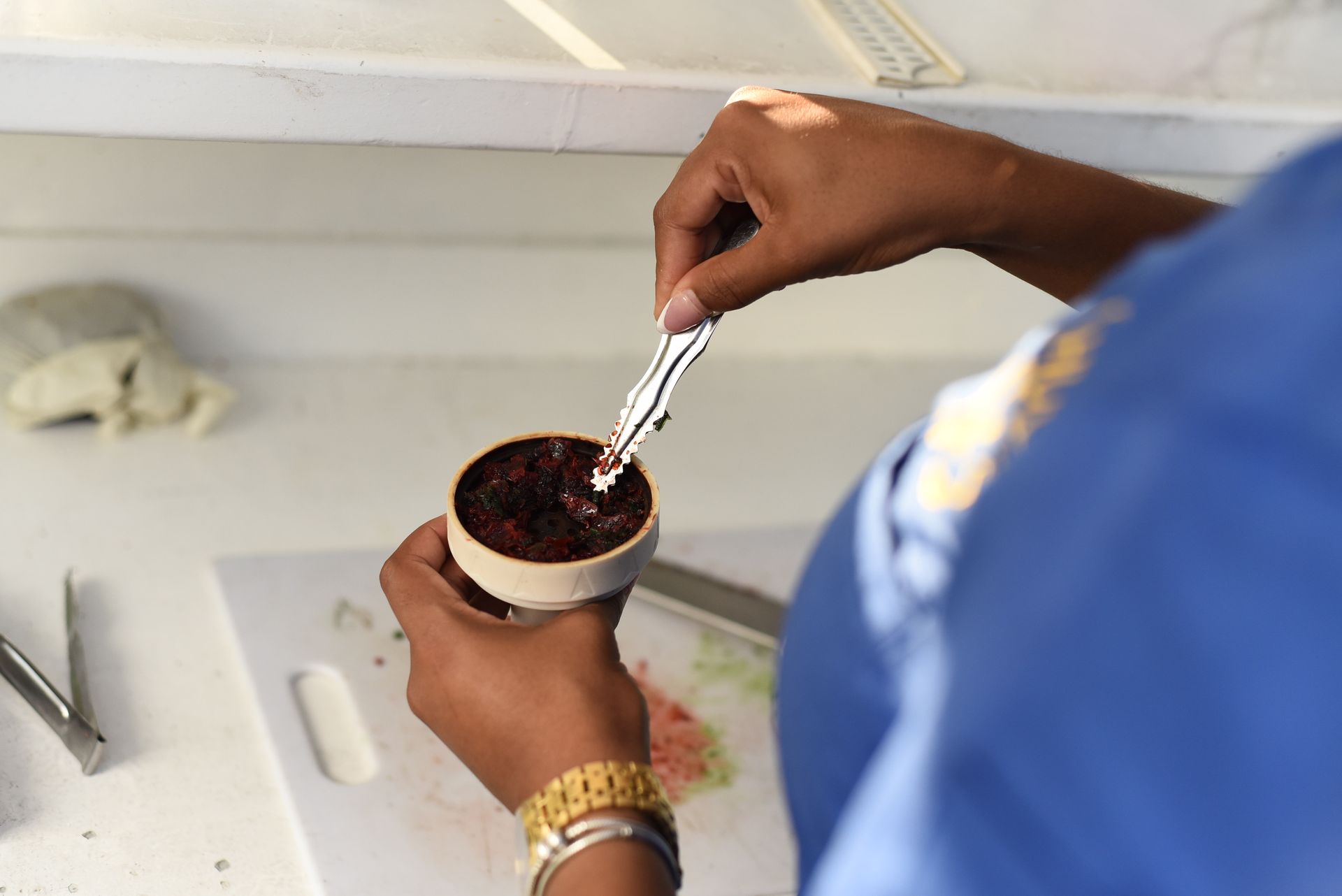 Person in blue shirt scoops a dark, reddish substance from a small, white bowl with a silver spoon.