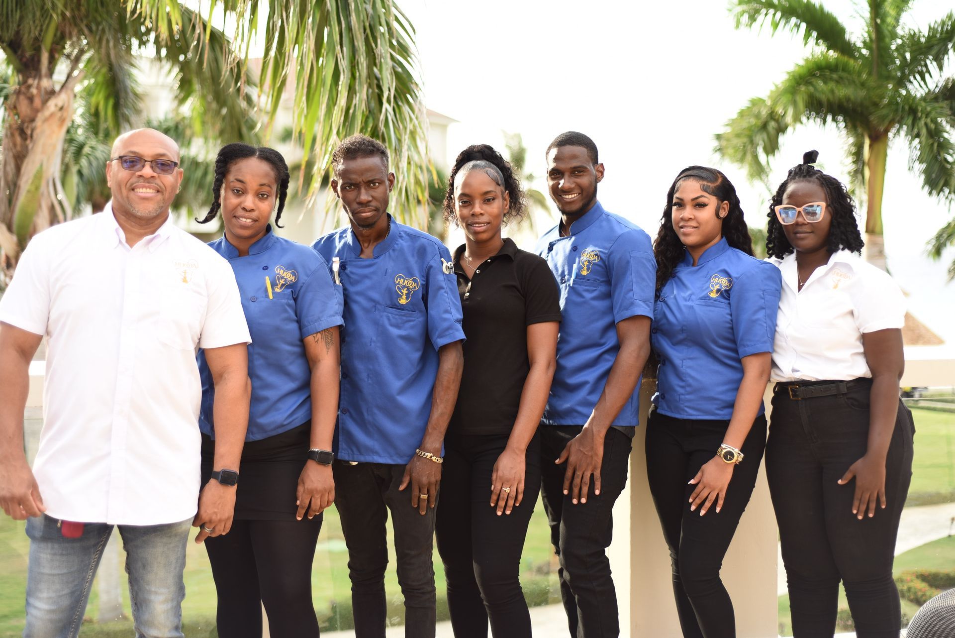 Group of people smiling outdoors, some wearing blue uniforms, others in casual clothes.
