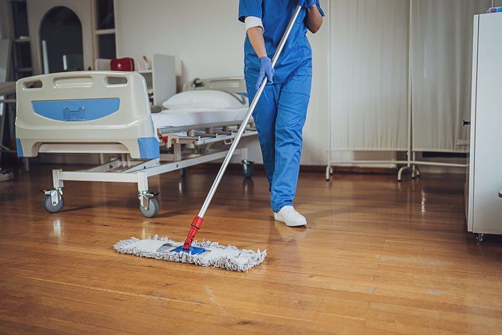 A nurse is cleaning the floor of a hospital room with a mop.