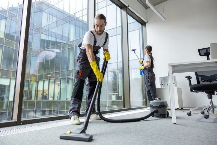 A man is cleaning the floor of an office with a vacuum cleaner.