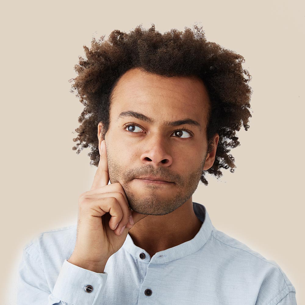 A man with curly hair is thinking with his hand on his chin.