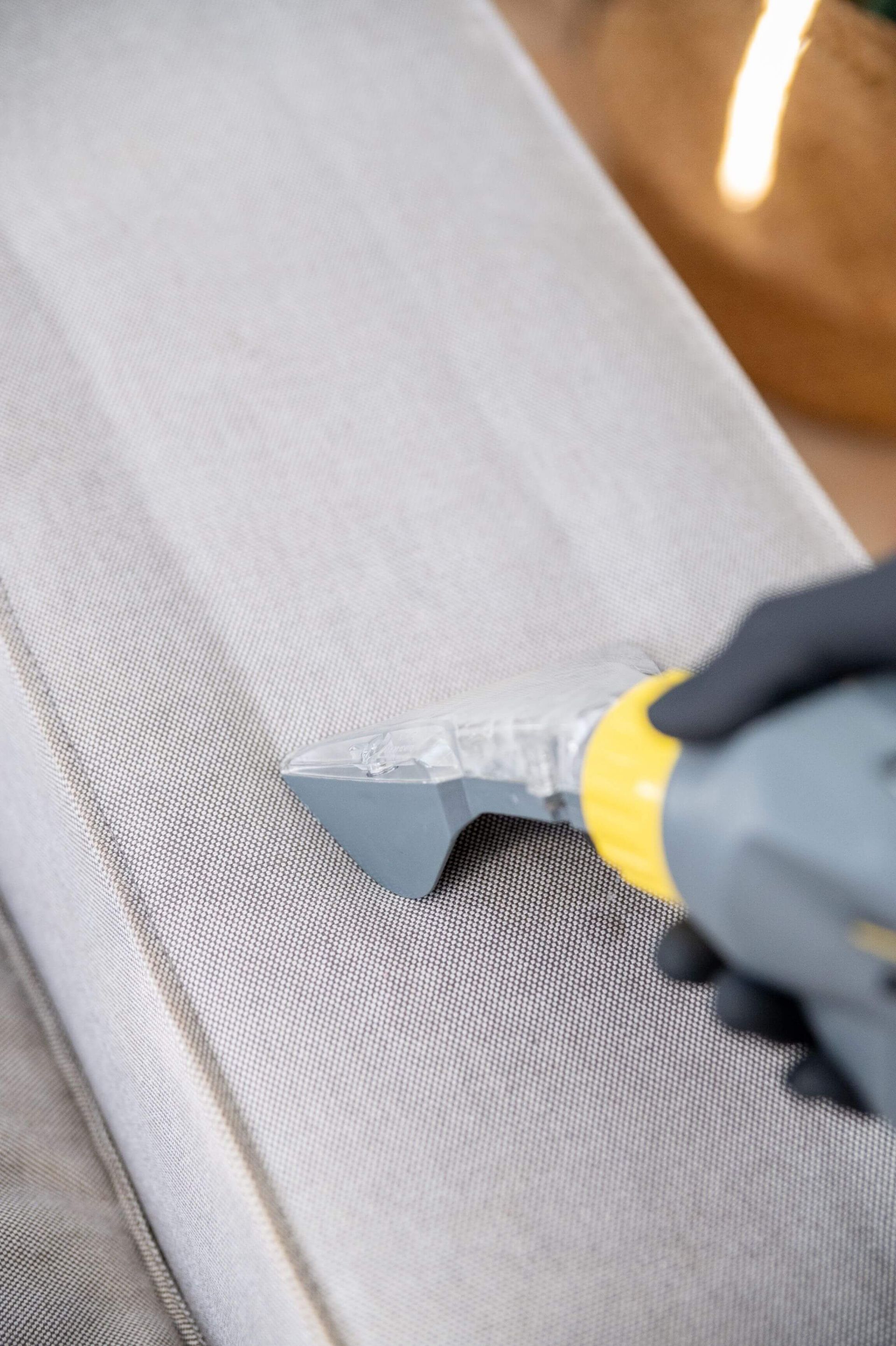 Un hombre está limpiando un sofá con una aspiradora.