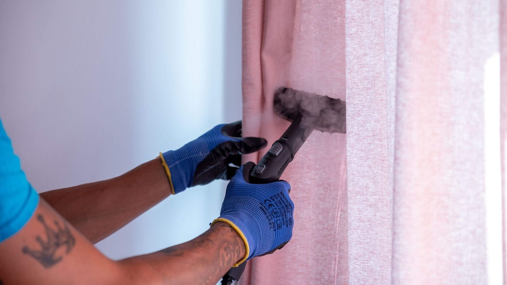 Un hombre está limpiando cortinas con una aspiradora.