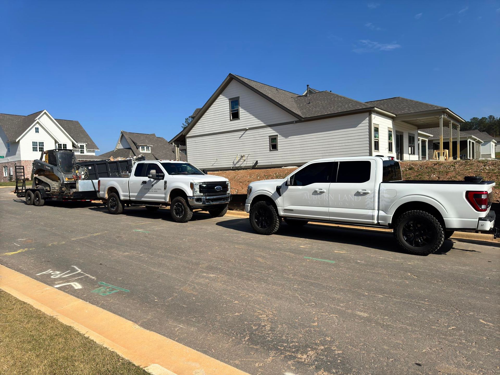 Three white trucks are parked on the side of the road in front of a house.