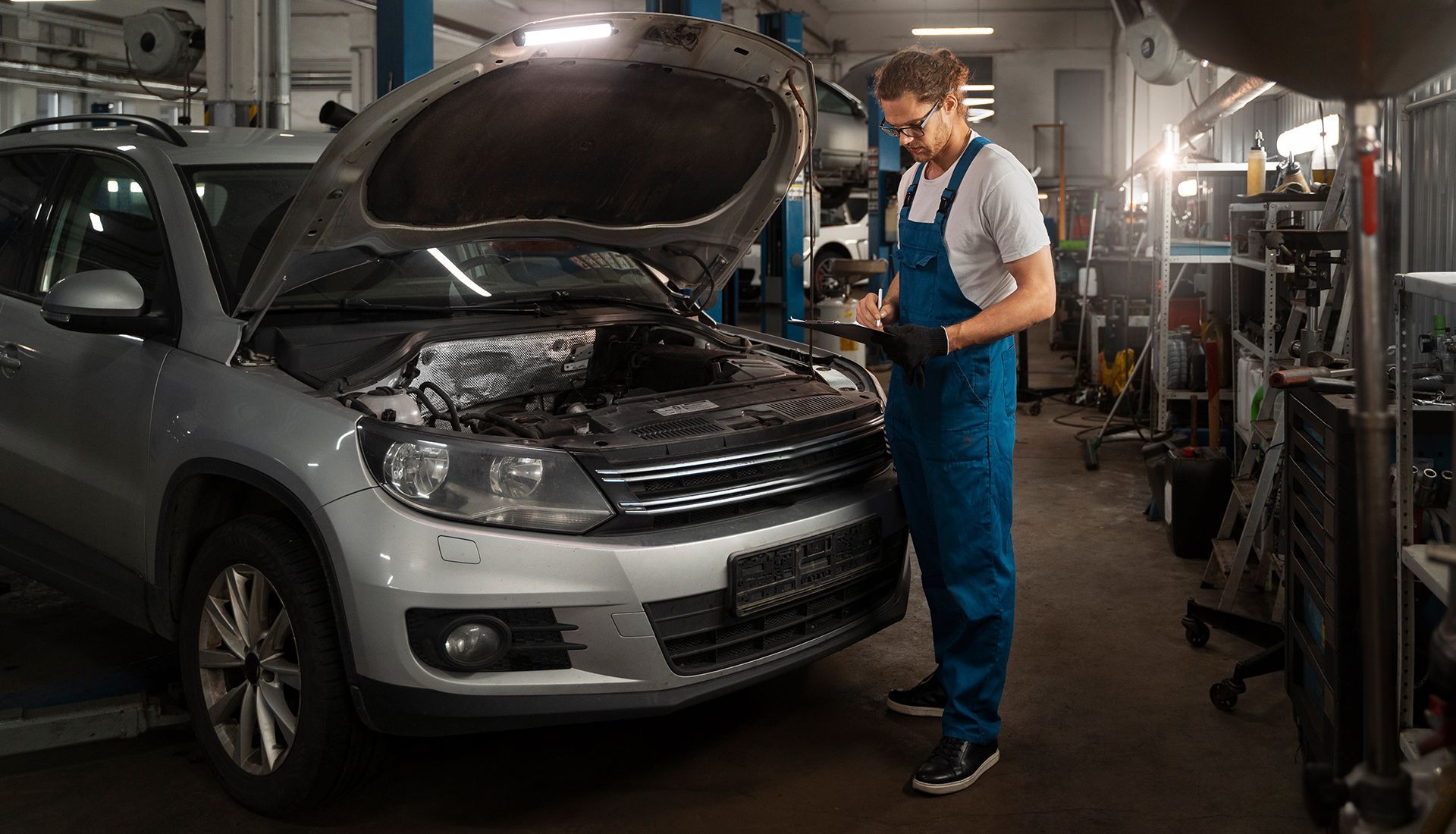 Mechanic inspecting a silver SUV with the hood open in an auto repair shop.