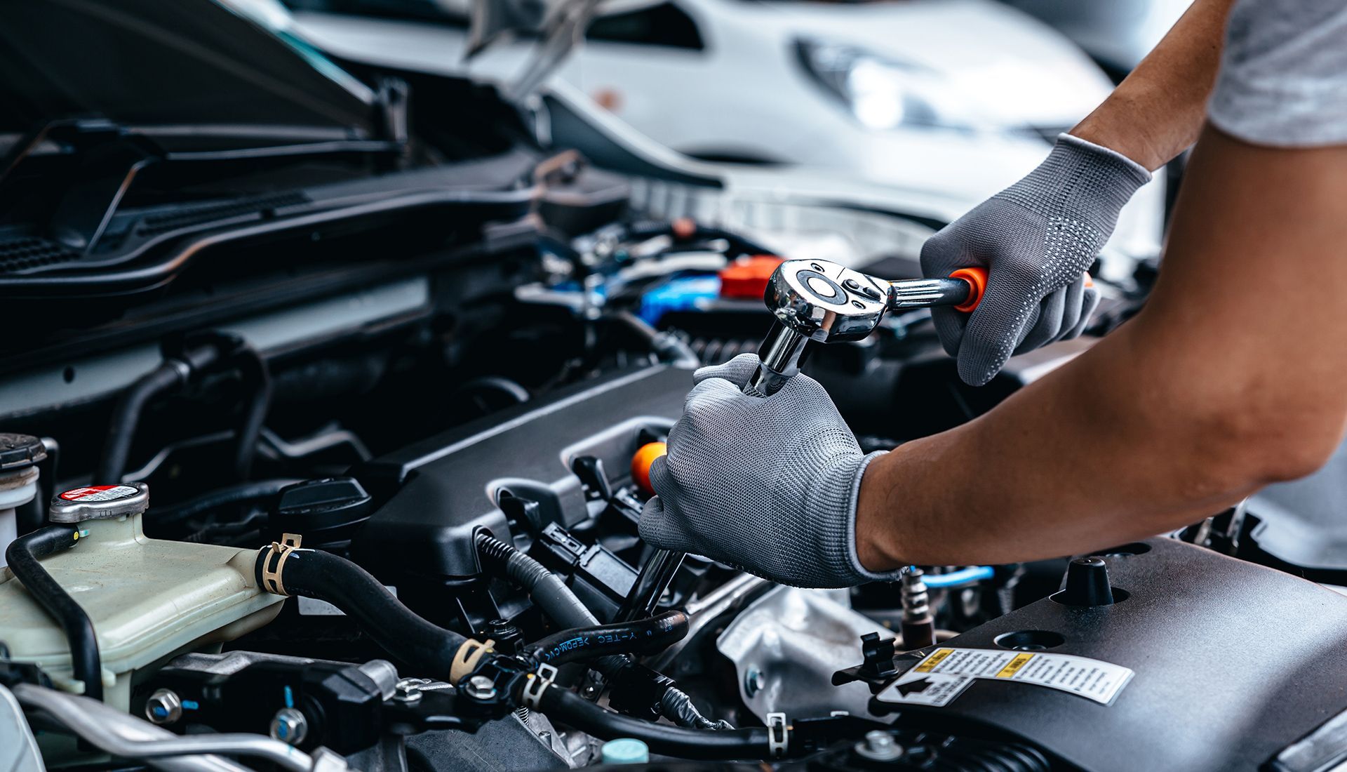 Mechanic working on a car engine with a wrench. Hands are gloved, working inside the hood.