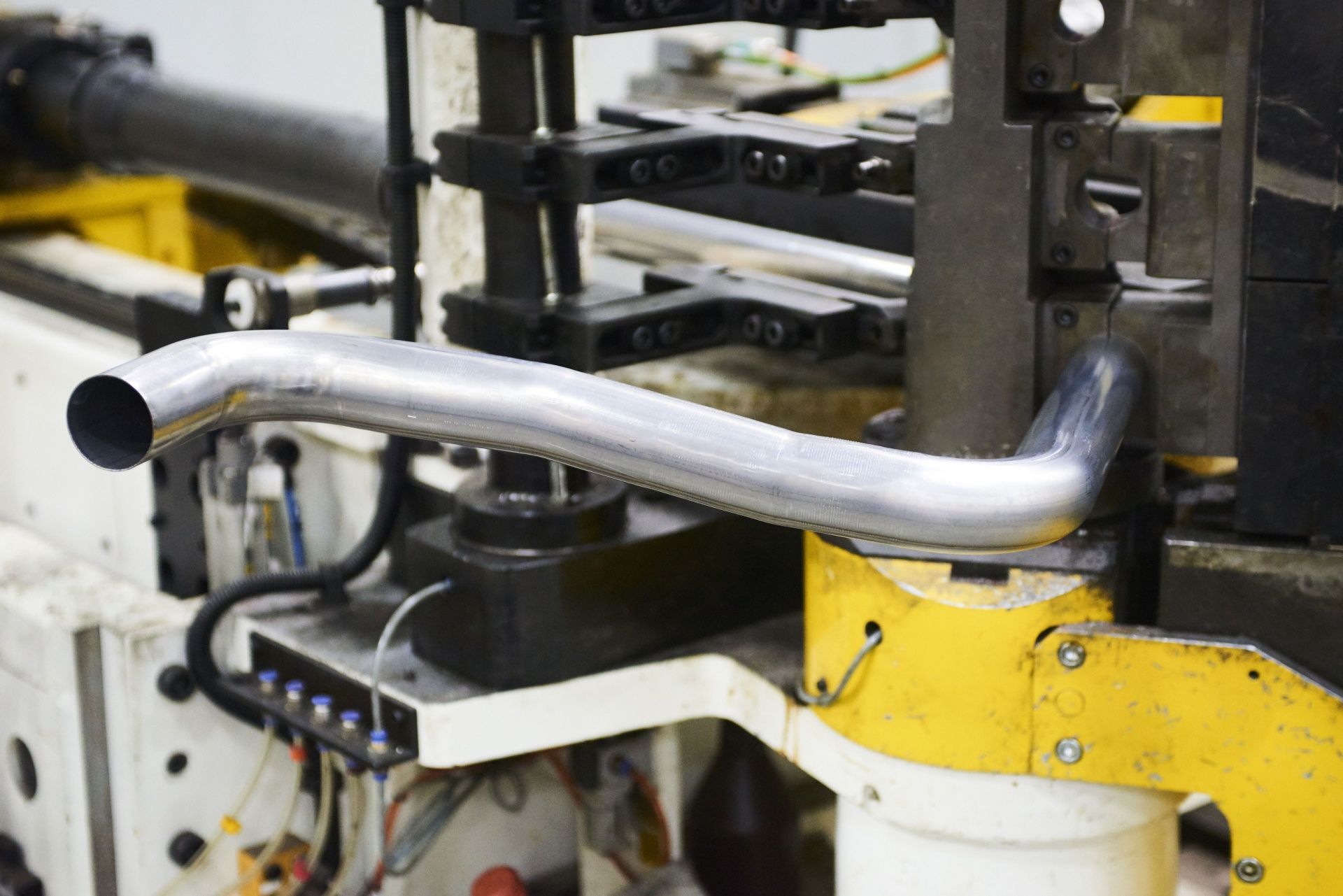 Metal pipe being bent by a machine in a factory setting.