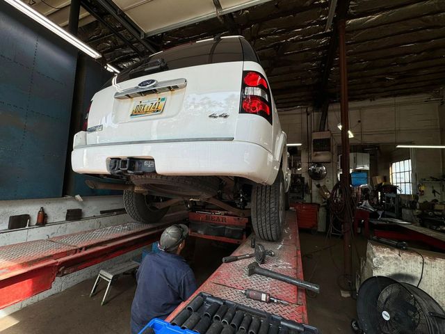 A white SUV on a lift in a garage, a mechanic works underneath.