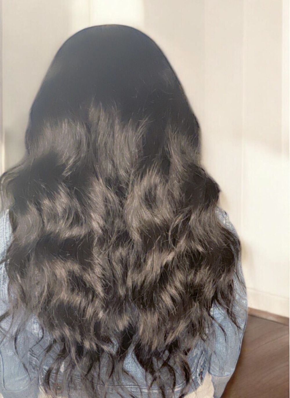 A woman wearing a wig and a denim jacket is smiling.