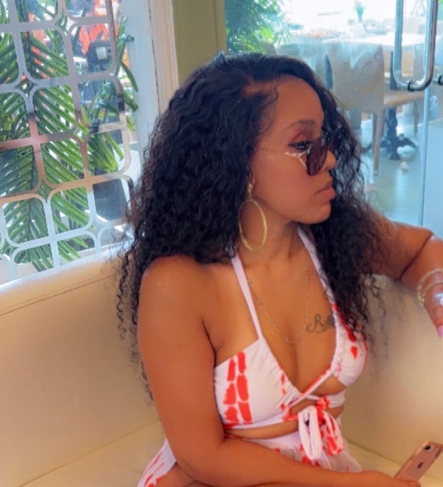 A woman in a bikini is sitting on a couch looking at her phone.