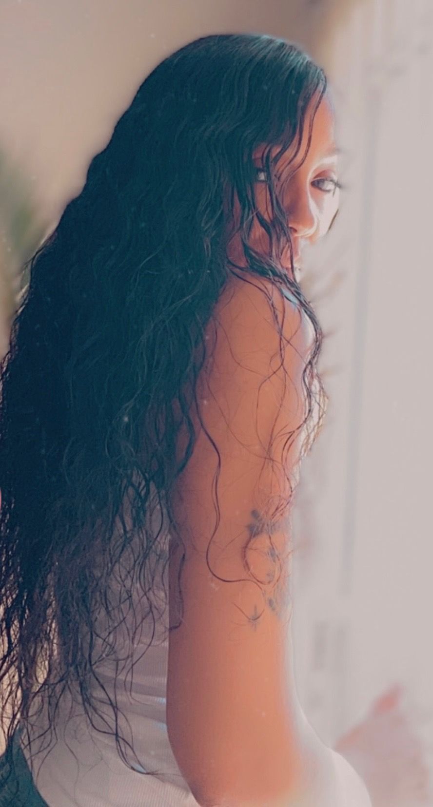 A woman with long black hair is sitting on a bed.